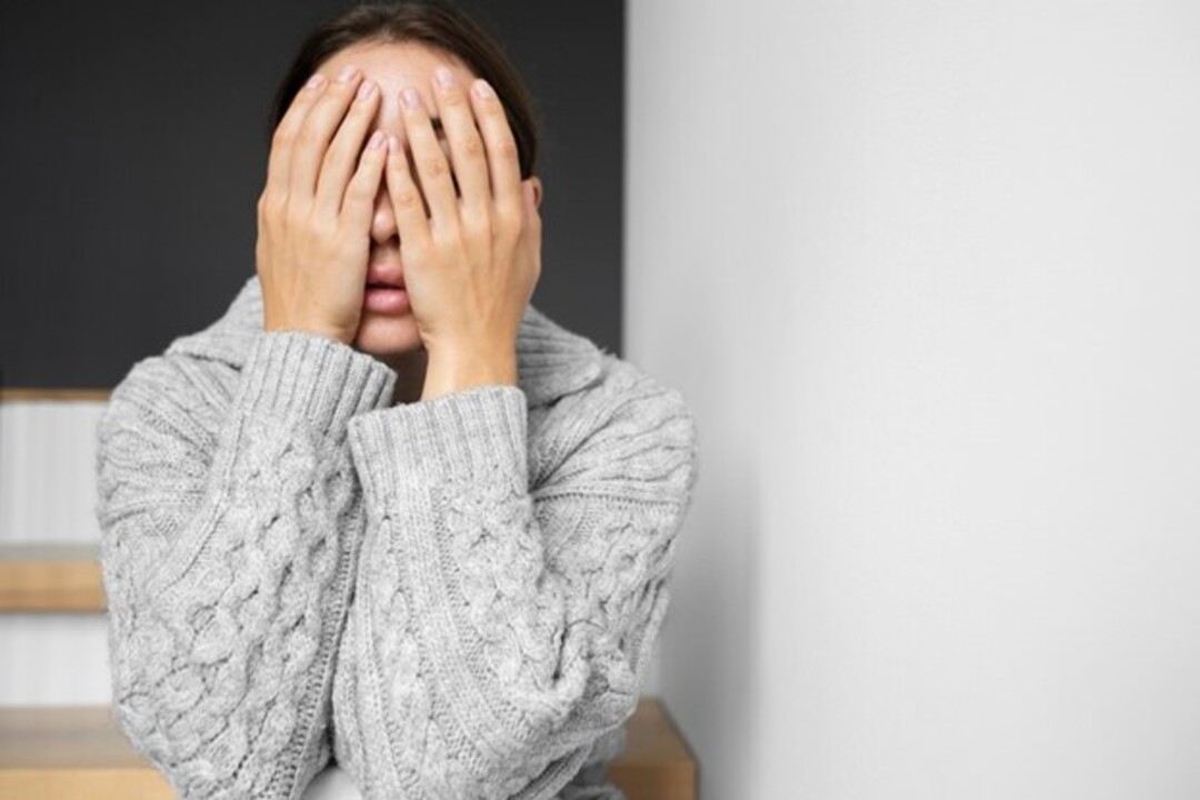 A person covering her face with her handsDescription automatically generated